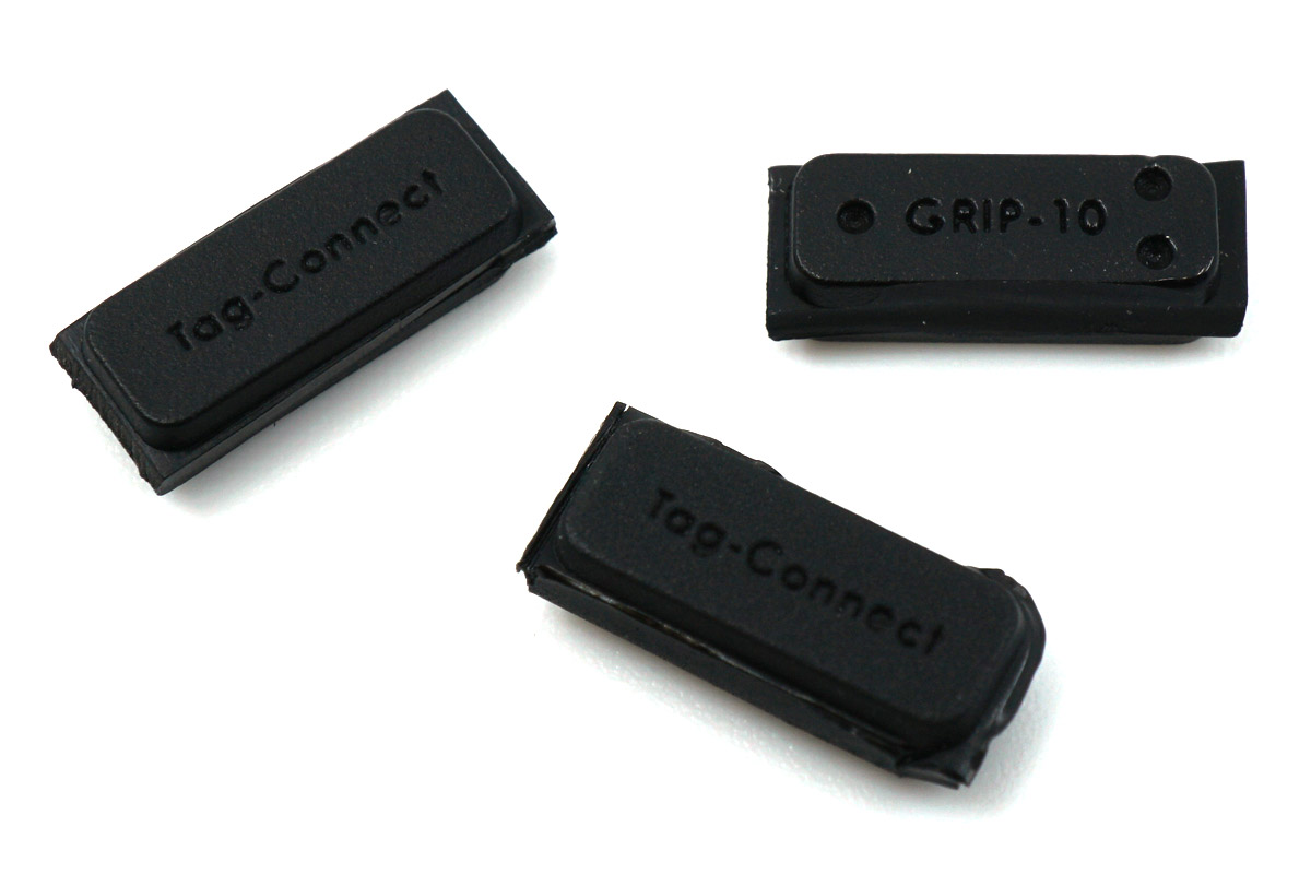 Drei GRIP-10 aus schwarzem Polymer, wie sie im 3er-Pack geliefert werden: flache Riegel mit zwei Bohrungen, die von der Platinenunterseite auf die Führungsstifte des zehnpoligen Kabels greifen.